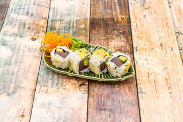 Sushi uramaki roll stuffed with red tuna and ripe avocado with green leaf-shaped plate