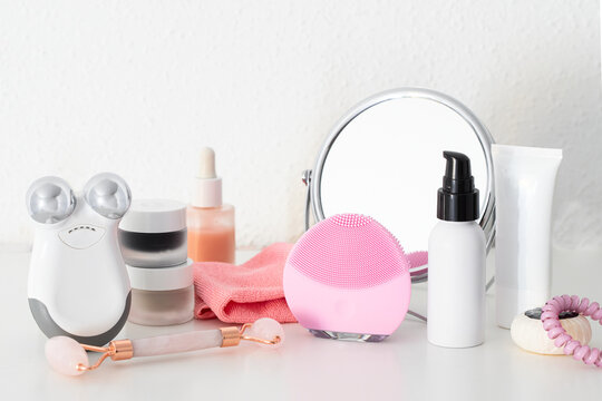 Modern beauty routine with gadgets. Cleanser and Microcurrent devices, Gua Sha roller, professional cleansing cloths , natural oil and serum, cream and masks on white table with mirror.