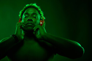 Black man in red wireless headphones listens to music and enjoys music on a black background in the...