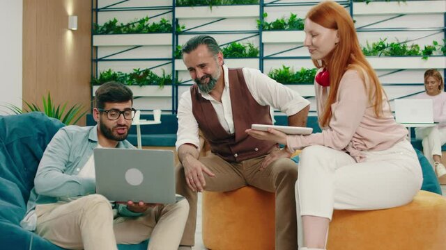 Three colleagues are having an interesting conversation about work while looking at the man in a bean bag chair holding a laptop