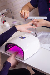 Female hand with manicure nails in gel polish lamp in beauty salon