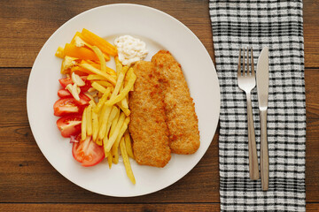 Traditional fish and chips on white plate with fresh cut tomatoes. Simple meal serving. Sea food.