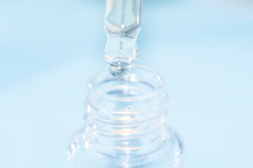 detail of face serum pouring out of pipette over a bottle on a blue background