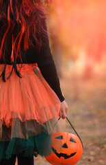 Little girl in witch costume with a balloon and a pumpkin bucket playing in autumn park. Child...