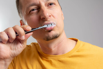 health care, dental hygiene, people - close up of middle aged man with toothbrush cleaning teeth. man brushing his teeth isolated on grey background. Morning routine of washing the teeth.