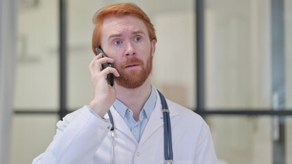 Redhead Male Doctor Talking on Smartphone at Work 