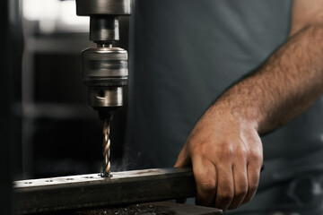 Competent craftsman doing holes in metal sheet using drill press. Close up of working manual...
