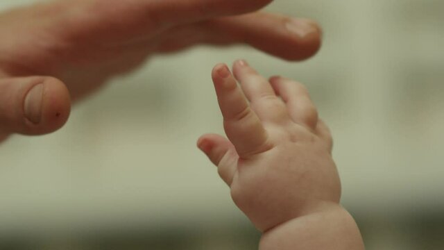 Close-up shot of baby's little cute hand reaching for father's loving finger . Baby holding parent's finger . Parent holding newborns hand in Slow Motion . Hand in hand. Father and his newborn baby . 