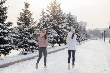 Two young athletic girls running in the park on a sunny winter day. A healthy way of life.