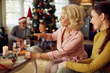 Senior woman pours wine while celebrating Christmas with her family at home.