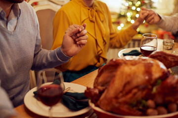Close-up of grateful family holds hands and prays during Christmas meal at dining table.