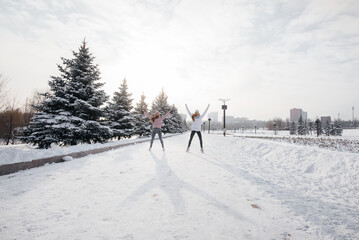 Two young athletic girls do a warm-up before running on a sunny winter day. A healthy way of life.