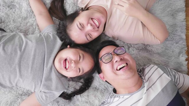 Top view of happy Asian family lying on the floor in living room, looking at camera and laughing together. Staying with family at home in the weekend. Happy family concept
