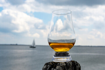 Tasting of dram single malt scotch whisky on seashore in Scotland, old wooden pole with whisky glass