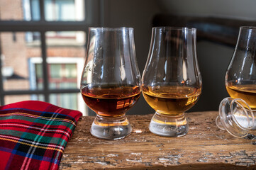 Dram of single malt scotch whisky served in tasting glass with view on old window and houses and red tartan