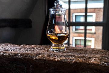 Dram of single malt scotch whisky served in tasting glass with view on old window and houses