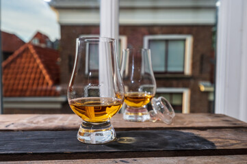 Dram of single malt scotch whisky served in tasting glass with view on old window and houses