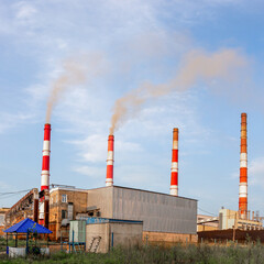 Fototapeta na wymiar Industrial landscape with smoking chimneys of plant against blue sky background. Air environment pollution