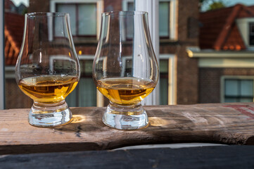 Dram of single malt scotch whisky served in tasting glass with view on old window and houses