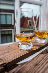 Dram of single malt scotch whisky served in tasting glass with view on old window and houses