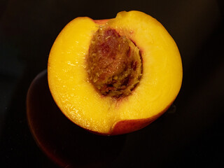 Half of an orange peach with a bone lies on black glass