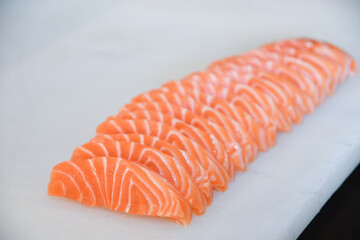Salmon sashimi lined up on a white board. © Kamol