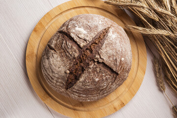 Overhead view of homemade rye black bread and spikelets of rye on a light wooden table.