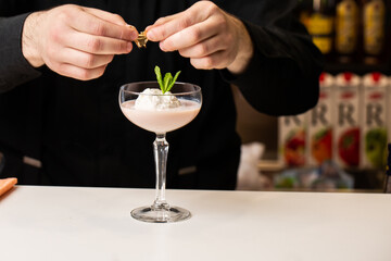 Male bartender decorates cocktail with ice cream and baileys in glass on bar counter