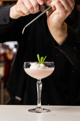 Male bartender rubs chocolate with a grater on a cocktail with ice cream and Baileys in a glass on the bar