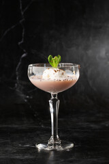 Glass of ice cold Baileys cocktail served in a coupe glass, decorated with mint leaf placed on a black background