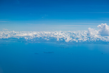 Aerial view scene of an island or coast in the big ocen which hiding under white fluffy clouds with bright blue sky background.