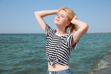 Fototapeta na wymiar Beautiful young woman near sea on sunny day in summer