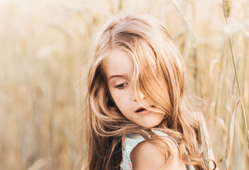 Naklejka premium Beautiful little girl blonde with long hair walking through a wheat field