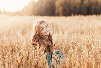 Portrait of a beautiful girl with long hair on a golden field at sunset