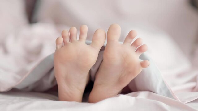 Close up Kid feet sticking out from under the blanket in the morning light. Child body legs in bed. Awakening Foot Sleep Relax Concept