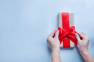 Hands tying a red ribbon on a present box