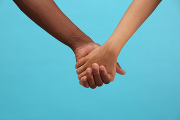 Woman and African American man holding hands on light blue background, closeup
