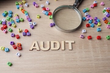 AUDIT from wooden font on the wooden table with a magnifying glass