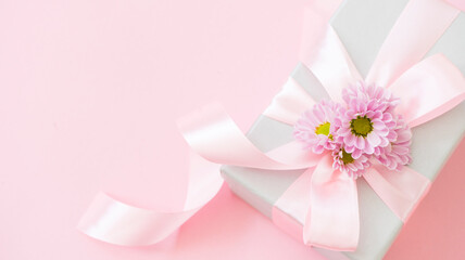 Beautiful gift box tied with a pink ribbon and decorated with flowers on a pink background