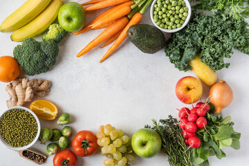 Variety of raw green vegetables salads, carrots, tomatoes, bananas, peas, corn, broccoli, savoy cabbage as frame round empty white chopping board. Food background. Top view, space for text