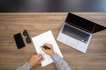 man's hand signing document, white paper with black and gold pen, wooden background.