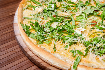Pizza with cheeses and herbs on a wooden plate. Close-up, selective focus