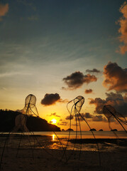 Colorful sunset on the beach. Reflection of the sunset sky in the water. Fishing nets in the form of jellyfish on the beach