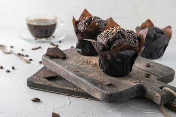 Chocolate muffins in dark craft paper on wooden boards. Pieces of chocolate and a cup of coffee in the background
