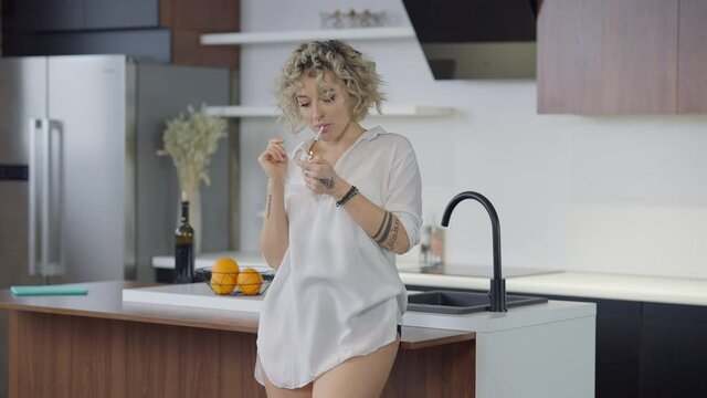 Confident slim beautiful woman lighting cigarette standing in kitchen at home. Portrait of gorgeous attractive Caucasian lady smoking indoors in slow motion. Lifestyle and harmful habits concept