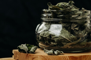 Dry mint leaves in a glass jar on a black background. Jar with mint on a wooden table. Mint for medicinal tea.