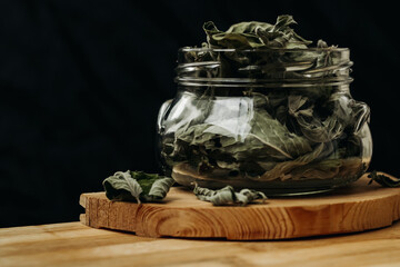 Dry mint leaves in a glass jar on a black background. Jar with mint on a wooden table. Mint for medicinal tea.