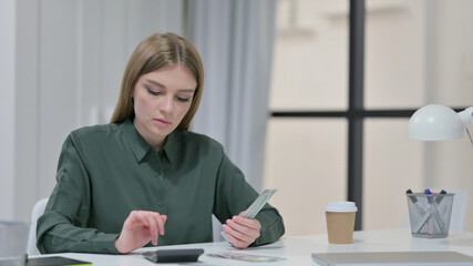 Young Woman using Calculator while Counting Dollars 