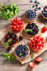 Tasty tartlets with berries on wooden table, top view.