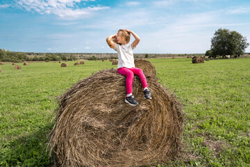 Naklejka na ściany i meble Little girl with long blonde hair in a field with hay rolls